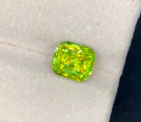 A cushion-cut bright yellow-green Sphene gemstone with iridescent flashes,